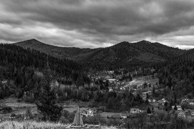 Sonbahar ormanlarındaki Karpatlar köyünün üzerinde siyah ve beyaz bulutlar