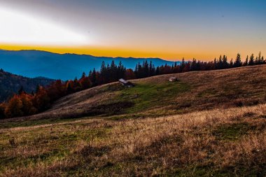 Sonbahar dağlarında gün batımı, ağaçlar ve çayırlarla dolu renkli sonbahar manzarası.
