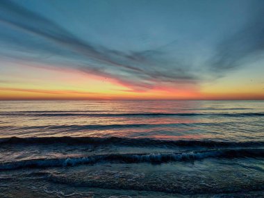 Sahilde dalgalarla denizin üstünde renkli bir gün batımı..