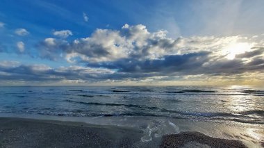 Güzel bir deniz manzarası, kumsalda bulutlu bir gün batımı.