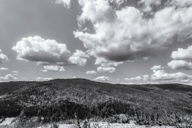Dağların üzerinde siyah ve beyaz bulutlar ve mavi gökyüzü