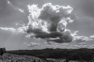 Gri tonlu güzel bulutlu bir günün görüntüsü bir dağın ortasında, önünde beyaz bir bulut var.