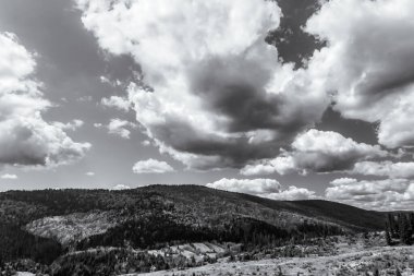 Siyah ve beyaz bulutlar ve arka planda dağlar.
