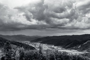 Dağların bulutlu gökyüzü ile çekilmiş siyah beyaz bir fotoğrafı.