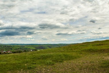 bulutlu bir gün manzarası, yeşil çimenler ve arka planda bulutlu bir gökyüzü.