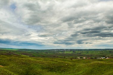 Tepelerin yeşil tarlaları ve bulutlu mavi gökyüzü