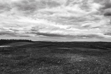 Arkasında bulutlu güzel bir gökyüzü olan bir yolun gri tonlu görüntüsü.