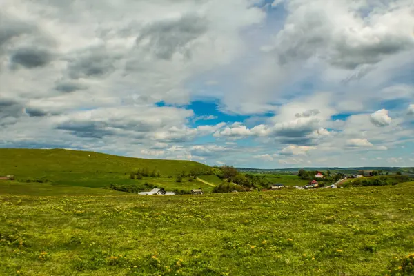 Mavi gökyüzü, beyaz bulutlar ve küçük yeşil bir çayır.