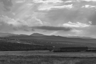 Arkasında bulutlu bir gökyüzü olan bir dağ manzarasının güzel gri tonlu görüntüsü.