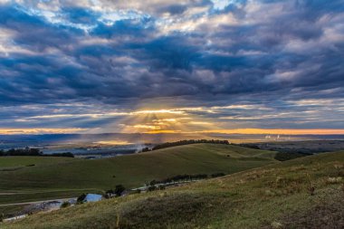 a vertical shot of the sunset in the middle of the field with colorful clouds