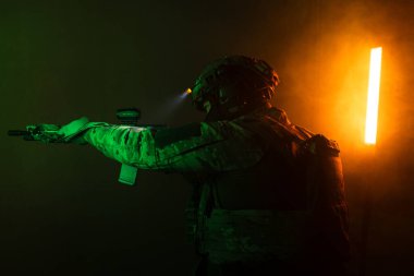 Üniformalı asker. Yüksek kaliteli 4K görüntüler. Tam teçhizatlı kararlı bir asker dumanlı, atmosferik bir sahnede yürüyor. Yoğun ve renkli ışıklandırmayla aydınlatılıyor.. 