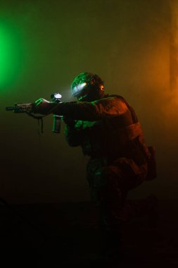 Üniformalı asker. Yüksek kaliteli 4K görüntüler. Tam teçhizatlı kararlı bir asker dumanlı, atmosferik bir sahnede yürüyor. Yoğun ve renkli ışıklandırmayla aydınlatılıyor.. 