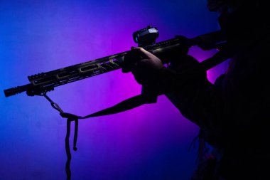 Üniformalı asker. Yüksek kaliteli 4K görüntüler. Tam teçhizatlı kararlı bir asker dumanlı, atmosferik bir sahnede yürüyor. Yoğun ve renkli ışıklandırmayla aydınlatılıyor.. 