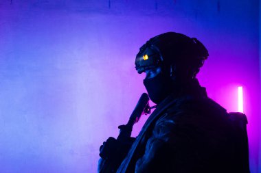 Üniformalı asker. Yüksek kaliteli 4K görüntüler. Tam teçhizatlı kararlı bir asker dumanlı, atmosferik bir sahnede yürüyor. Yoğun ve renkli ışıklandırmayla aydınlatılıyor.. 