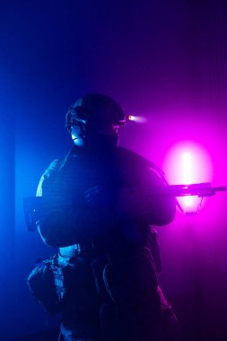 Üniformalı asker. Yüksek kaliteli 4K görüntüler. Tam teçhizatlı kararlı bir asker dumanlı, atmosferik bir sahnede yürüyor. Yoğun ve renkli ışıklandırmayla aydınlatılıyor.. 