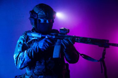 Üniformalı asker. Yüksek kaliteli 4K görüntüler. Tam teçhizatlı kararlı bir asker dumanlı, atmosferik bir sahnede yürüyor. Yoğun ve renkli ışıklandırmayla aydınlatılıyor.. 