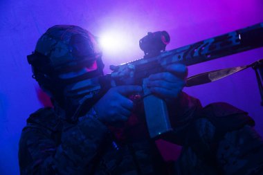 Üniformalı asker. Yüksek kaliteli 4K görüntüler. Tam teçhizatlı kararlı bir asker dumanlı, atmosferik bir sahnede yürüyor. Yoğun ve renkli ışıklandırmayla aydınlatılıyor.. 