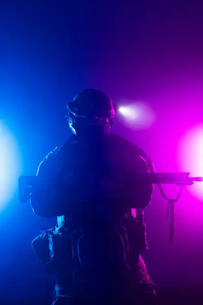 Üniformalı asker. Yüksek kaliteli 4K görüntüler. Tam teçhizatlı kararlı bir asker dumanlı, atmosferik bir sahnede yürüyor. Yoğun ve renkli ışıklandırmayla aydınlatılıyor.. 