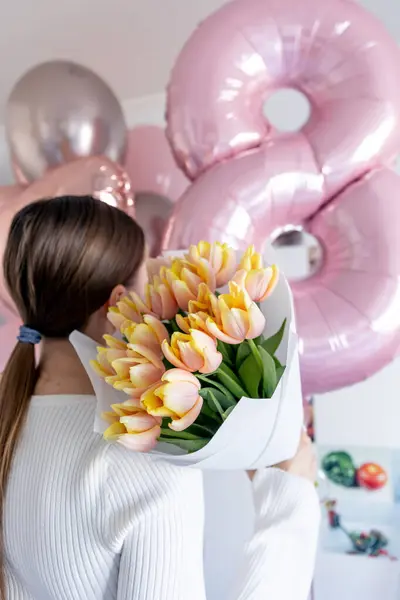 Genç bir kadın elinde pembe kenarlı taze sarı lalelerden oluşan bir buket tutuyor. Güzelce beyaz kağıda sarılmış..