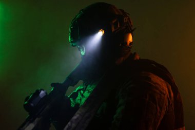 Üniformalı asker. Yüksek kaliteli 4K görüntüler. Tam teçhizatlı kararlı bir asker dumanlı, atmosferik bir sahnede yürüyor. Yoğun ve renkli ışıklandırmayla aydınlatılıyor.. 