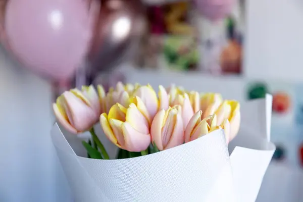 Genç bir kadın elinde pembe kenarlı taze sarı lalelerden oluşan bir buket tutuyor. Güzelce beyaz kağıda sarılmış..