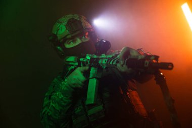 Üniformalı asker. Yüksek kaliteli 4K görüntüler. Tam teçhizatlı kararlı bir asker dumanlı, atmosferik bir sahnede yürüyor. Yoğun ve renkli ışıklandırmayla aydınlatılıyor.. 