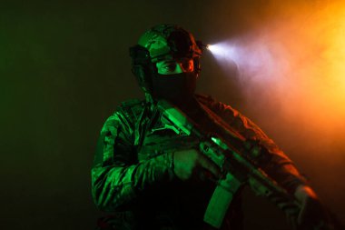 Üniformalı asker. Yüksek kaliteli 4K görüntüler. Tam teçhizatlı kararlı bir asker dumanlı, atmosferik bir sahnede yürüyor. Yoğun ve renkli ışıklandırmayla aydınlatılıyor.. 