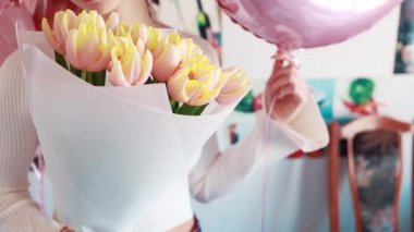 Genç bir kadın elinde pembe kenarlı taze sarı lalelerden oluşan bir buket tutuyor. Güzelce beyaz kağıda sarılmış..