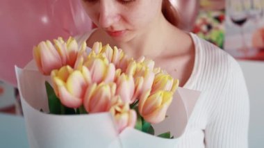 Genç bir kadın elinde pembe kenarlı taze sarı lalelerden oluşan bir buket tutuyor. Güzelce beyaz kağıda sarılmış..
