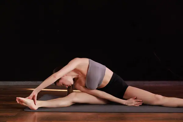 Yoga ve esneme hareketi Low Lunge PoseA 'da genç bir kadın yoga yapıyor ve kapalı alanda esniyor koyu gri bir paspasın üzerinde.. 