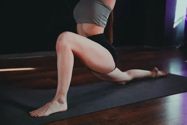 Yoga ve esneme hareketi Low Lunge PoseA 'da genç bir kadın yoga yapıyor ve kapalı alanda esniyor koyu gri bir paspasın üzerinde.. 