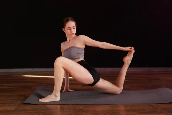 Yoga ve esneme hareketi Low Lunge PoseA 'da genç bir kadın yoga yapıyor ve kapalı alanda esniyor koyu gri bir paspasın üzerinde.. 