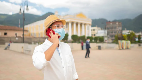 Portrait of a young man with a medical mask talking on a cell phone in front of a church.