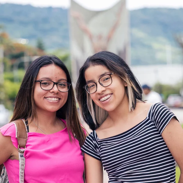 best friends posing on camera, latin-american girls wearing glasses and smile 
