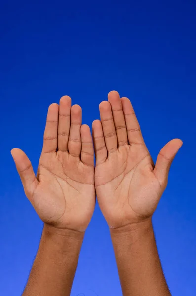 Empty hands showing palms, thanking, raised to the sky, on blue background