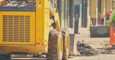 Sarı inşaat aracı binaların yakınında moloz taşıyor.