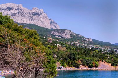 Sahili, yemyeşil yeşili, berrak mavi denizi ve güneşli bir gökyüzünün altındaki ağaçlık tepeleri olan bir tatil köyünün manzarası..