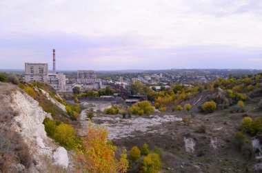 Tepeler ve sonbahar yapraklarıyla çevrili bir sanayi şehri, gazoz fabrikası bacaları ve bulutlu bir gökyüzünün altındaki yerleşim alanları.