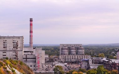 Ağaçlarla çevrili uzun bir bacası ve bulutlu bir gökyüzünün altındaki uzak tepeleri olan büyük bir endüstriyel soda fabrikası..