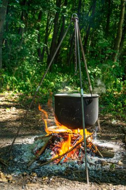Ağaçlık alanda yemek pişirmek için tripodun üzerinde asılı duran metal tencere.