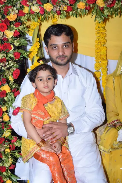 Beyaz elbiseli baba ve sarı ve turuncu elbiseli kız düğün törenine katılıyor. 