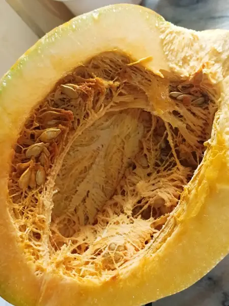 İkiye bölünmüş bir balkabağı parlak turuncu derisini gösterir. Ortadaki çekirdekleri ve yumuşak iplik parçalarını da görebilirsiniz..