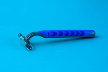 Mavi, tek kullanımlık, parlak mavi arka planda koruyucu kapaklı bir jilet. Ergonomik sapı ve keskin bıçak, yüz veya vücut kıllarını güvenli ve pürüzsüz tıraş etmek için ideal hale getirir.