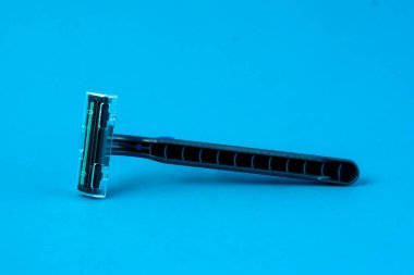 Mavi, tek kullanımlık, parlak mavi arka planda koruyucu kapaklı bir jilet. Ergonomik sapı ve keskin bıçak, yüz veya vücut kıllarını güvenli ve pürüzsüz tıraş etmek için ideal hale getirir.