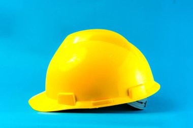 Mavi arka planda parlak sarı bir inşaat başlığı. Endüstriyel işçiler, mühendisler ve inşaatçılar için güvenlik kaskı, işyeri korumasını ve mesleki güvenliği sembolize ediyor.