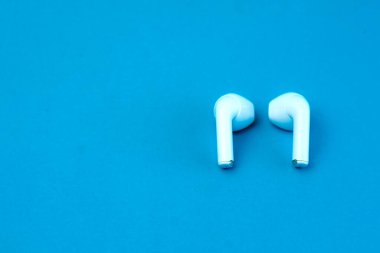 Canlı mavi bir arka planda bir çift modern kablosuz kulaklık. Yüksek kaliteli kulaklıklar, kusursuz bağlantılar ve günlük kolaylıklar için tasarlanmış şık ve kompakt kulaklıklar..