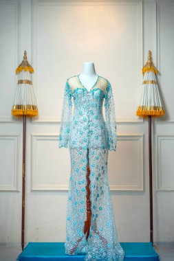 Saf dantelli, çiçekli, parlak boncuk işlemeli zarif, açık mavi kebaya bir manken, kadınlığı, zarafeti ve geleneksel güzelliği sembolize ediyor..