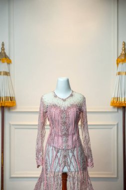 Işıldayan pullar ve narin boncuklarla süslenmiş pembe bir gelinlik geleneksel tören şemsiyeleriyle çerçevelenmiş bir mankenin üzerinde güzel bir şekilde sergileniyor..