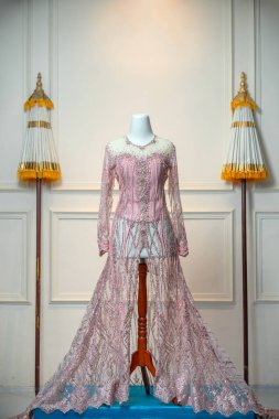 Geleneksel tören şemsiyeleri ve temiz ve zarif bir ortamda sergilenen, karışık pullu ve boncuk süslemeli, lüks pembe bir gelinlik..