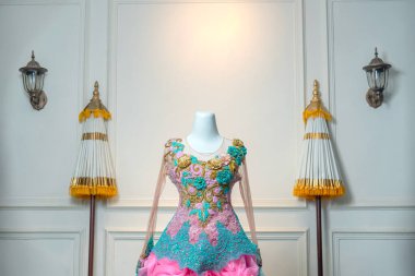 Karmaşık altın, turkuaz ve dantel işlemeli pembe çiçekli süslü bir balo elbisesinin yakın çekimi klasik bir iç dekordaki bir mankenin üzerinde zarif bir şekilde sergilendi..